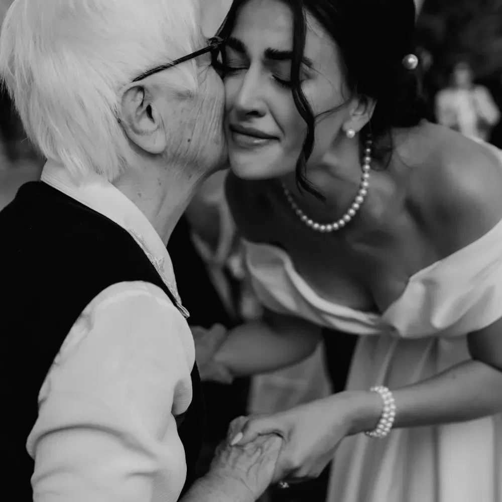 Emotionale Schwarz-Weiß-Aufnahme einer Braut, die liebevoll von ihrer Großmutter auf die Wange geküsst wird.