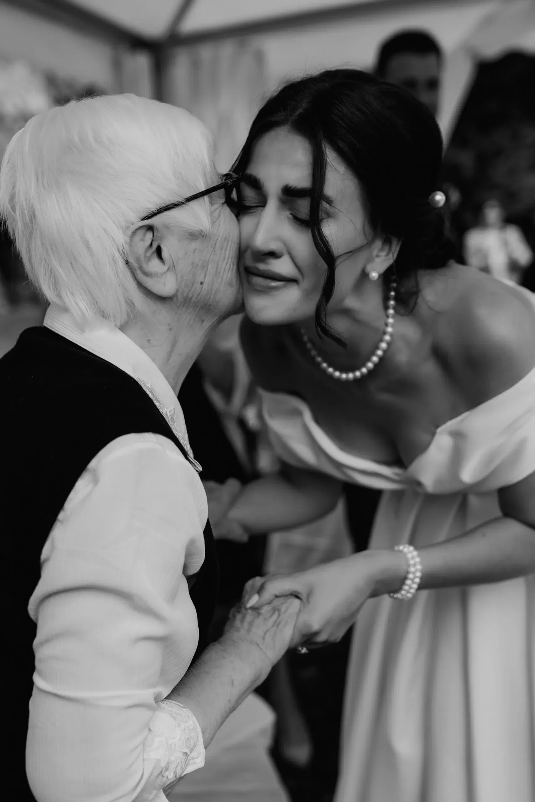 Emotionale Schwarz-Weiß-Aufnahme einer Braut, die liebevoll von ihrer Großmutter auf die Wange geküsst wird.