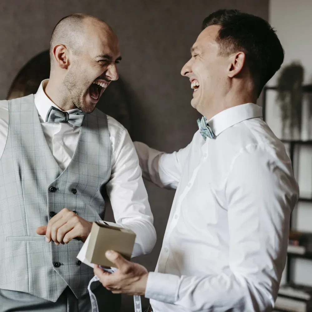 Zwei Männer in eleganter Hochzeitskleidung lachen herzlich beim Getting-ready.