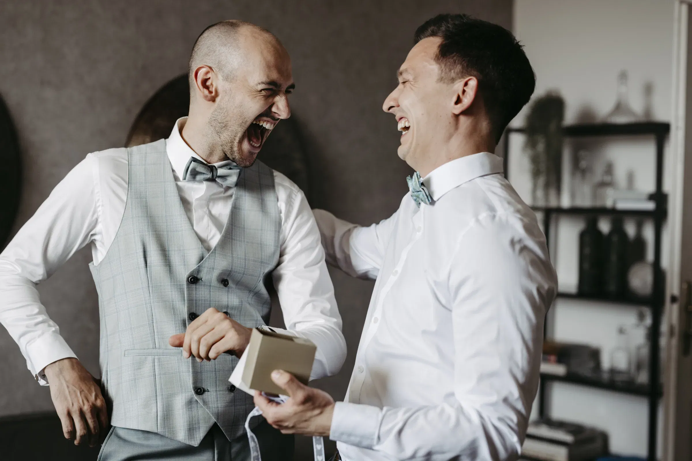 Zwei Männer in eleganter Hochzeitskleidung lachen herzlich beim Getting-ready.