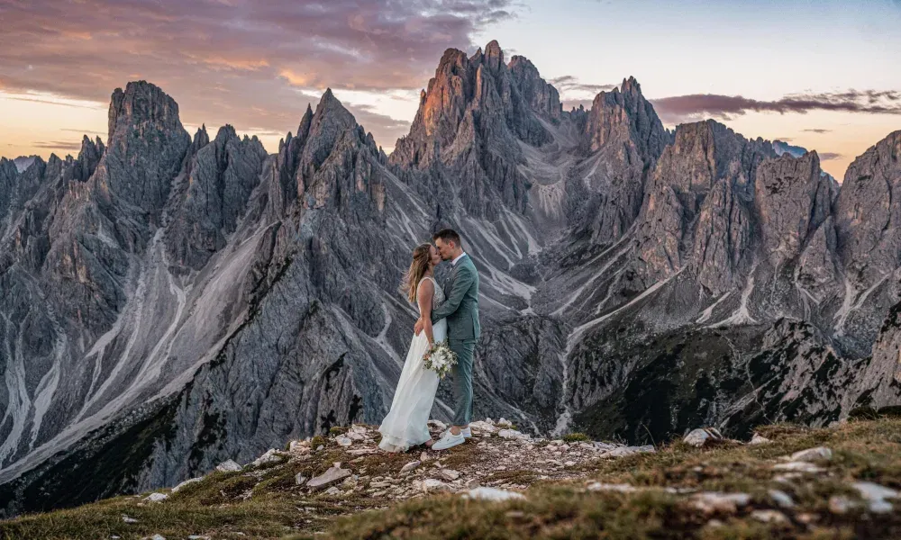 Ein Brautpaar küsst sich auf einem Bergplateau, umgeben von den dramatischen Felsformationen der Dolomiten im Abendlicht.