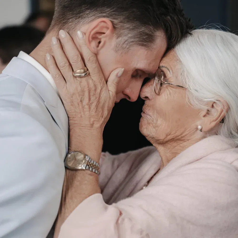 Emotionale Umarmung zwischen einem Bräutigam und einer älteren Angehörigen, die ihm mit beiden Händen das Gesicht hält.