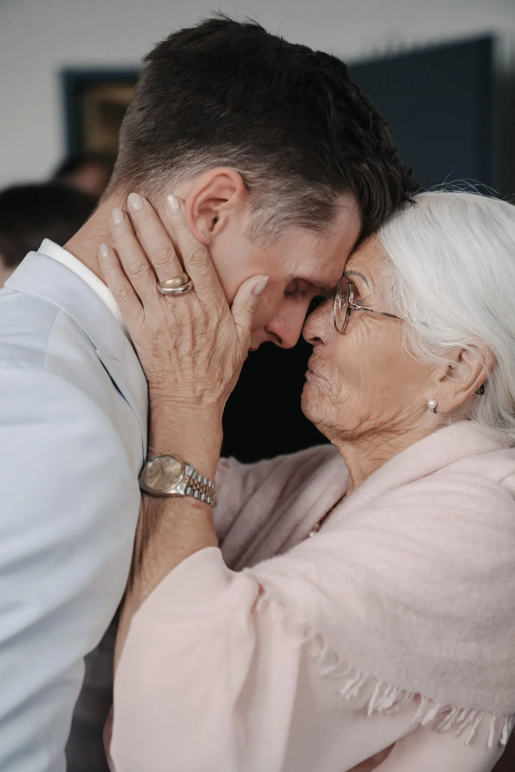Emotionale Umarmung zwischen einem Bräutigam und einer älteren Angehörigen, die ihm mit beiden Händen das Gesicht hält.