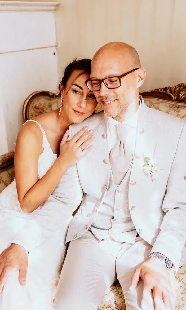 Braut und Bräutigam sitzen eng aneinander auf einem antiken Sofa, die Braut lehnt liebevoll ihren Kopf an seine Schulter.