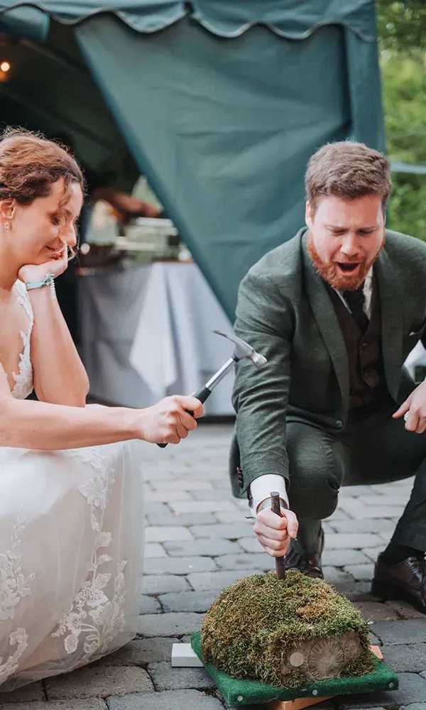 Das Paar kniet lachend neben einer moosbewachsenen Aufgabe und klopft mit kleinen Hämmern darauf ein.