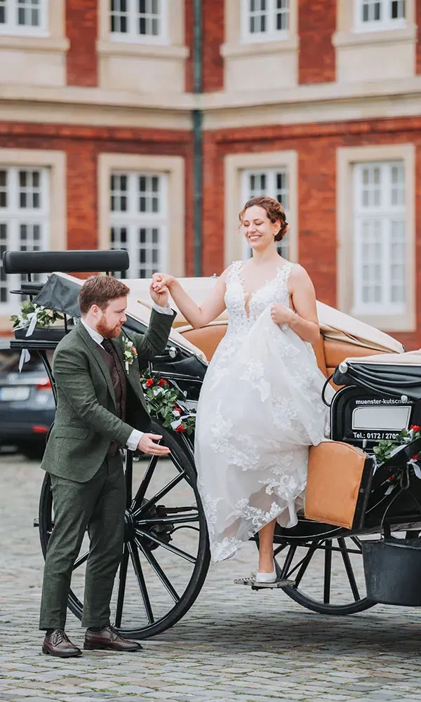 Eleganter Moment: Der Bräutigam begleitet die Braut vorsichtig beim Aussteigen aus der Hochzeitskutsche.