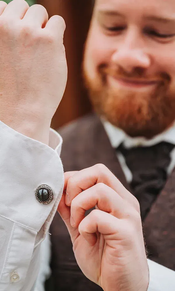 Detailshot: Der Bräutigam richtet seine verzierte Manschette und steckt den Knopf fest.