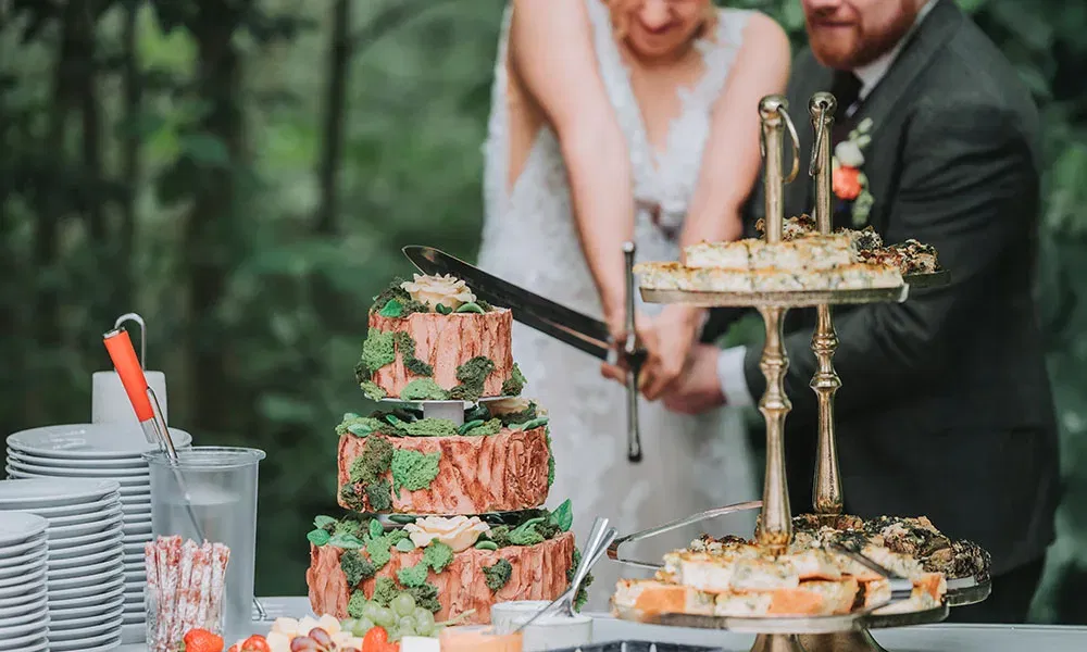 Braut und Bräutigam schneiden ihre Hochzeitstorte gemeinsam mit einem Schwert an.