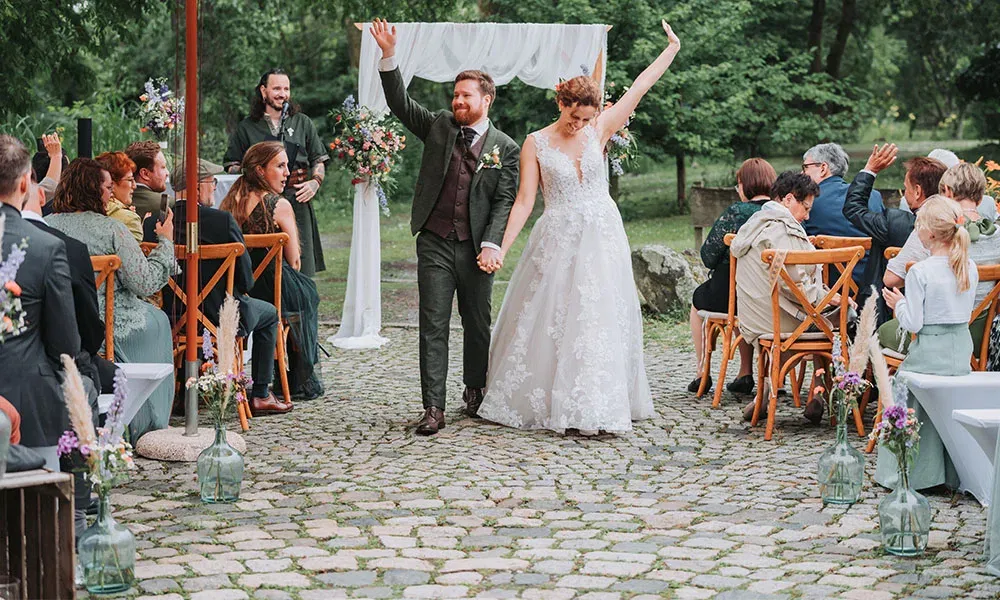Braut und Bräutigam laufen strahlend den Auszug entlang, während die Gäste jubeln und applaudieren.