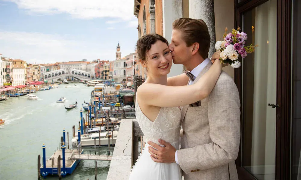 Glückliches Brautpaar auf einem Balkon mit Blick auf den Canal Grande, die Braut lächelt in die Kamera.