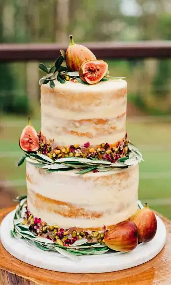 Zweistöckige Naked Cake Hochzeitstorte mit Feigen, Pistazien und Olivenzweigen dekoriert.