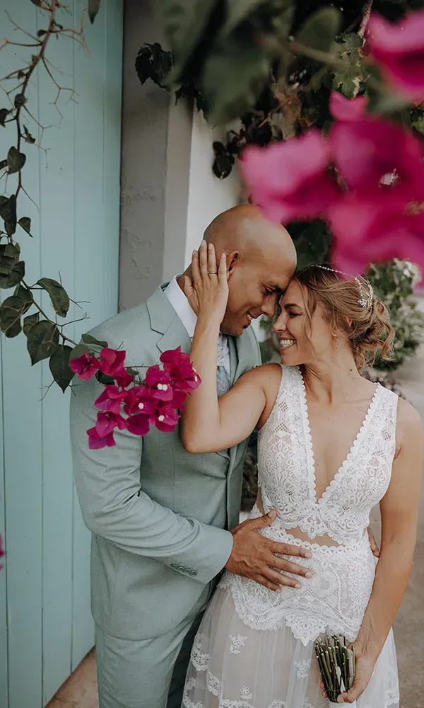 Romantische Szene: Die Braut hält das Gesicht des Bräutigams, während sie sich unter leuchtenden Blüten zärtlich anlehnen.