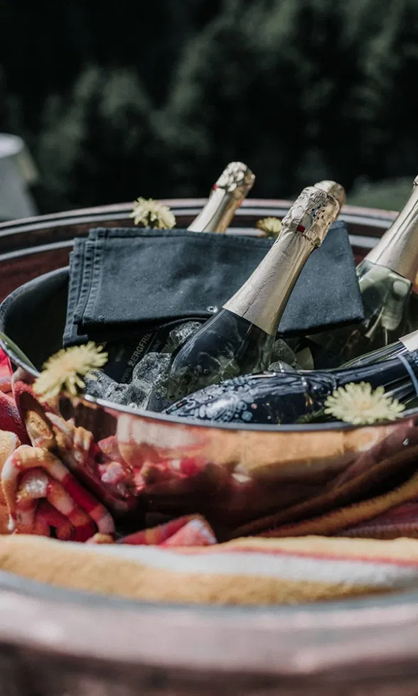 Hochzeitsgetränke im Outdoor-Bereich: Champagnerflaschen werden in einer Metallschale auf Eis gekühlt, dekoriert mit natürlichen Elementen.