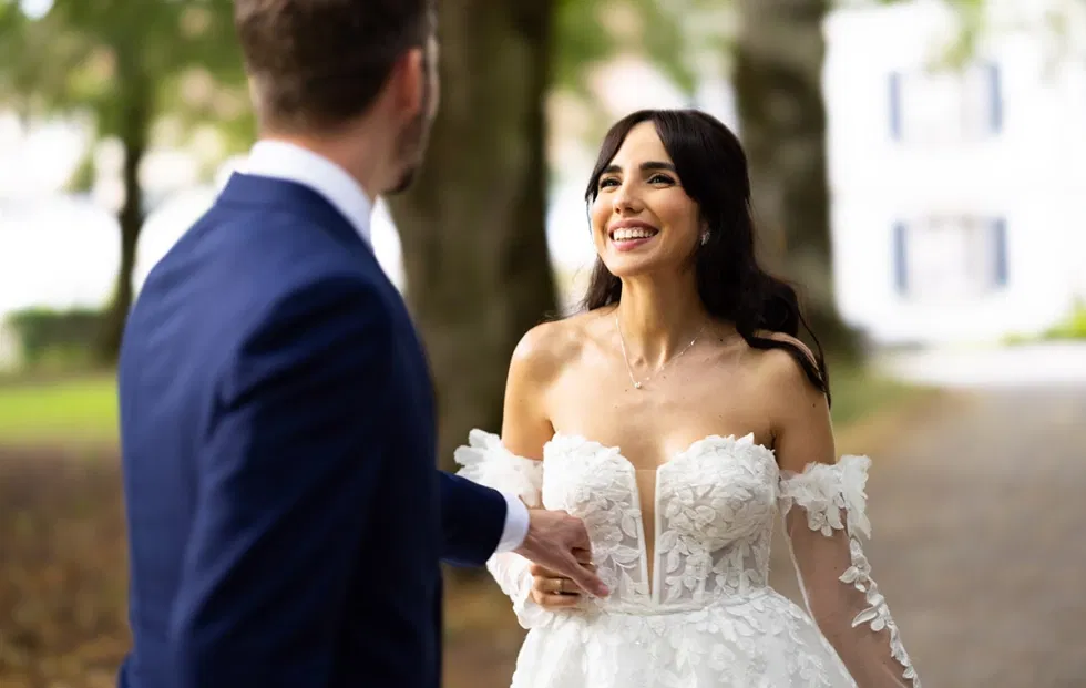 Braut und Bräutigam stehen sich im Schlosspark gegenüber und lächeln sich glücklich an, umgeben von sommerlicher Natur.