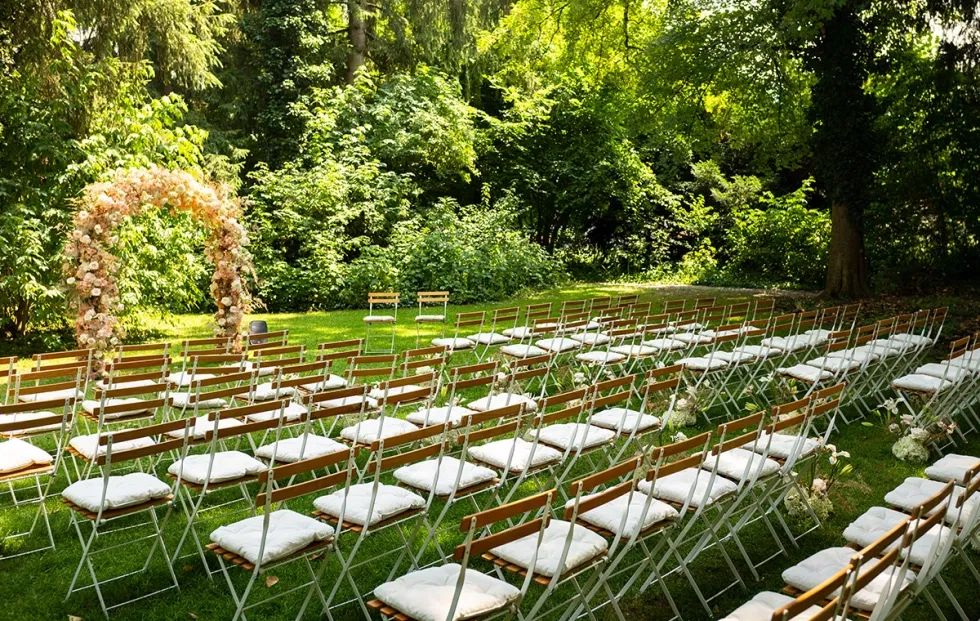 Freie Trauungsbestuhlung im Schlossgarten mit Blumenbogen und Stuhlreihen auf der Wiese, bereit für die Hochzeitszeremonie.