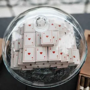 Gestapelte Spielkarten-Schachteln mit Herzmotiv unter einer Glasglocke als kreative Hochzeitsdeko.