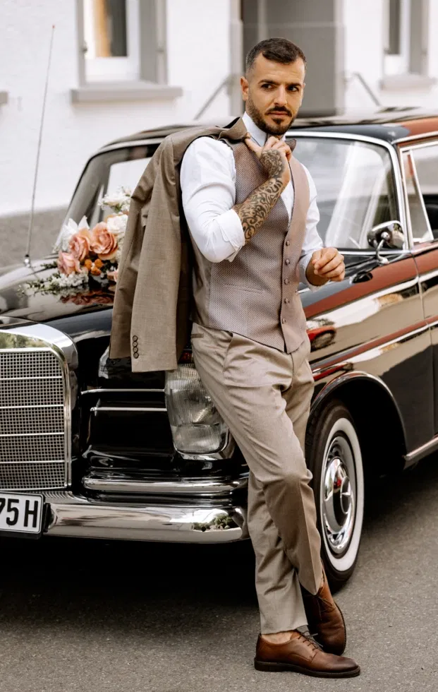 Bräutigam mit Jacke über der Schulter lehnt am Oldtimer-Mercedes mit Blumen – Hochzeitsauto im Vintage-Stil.