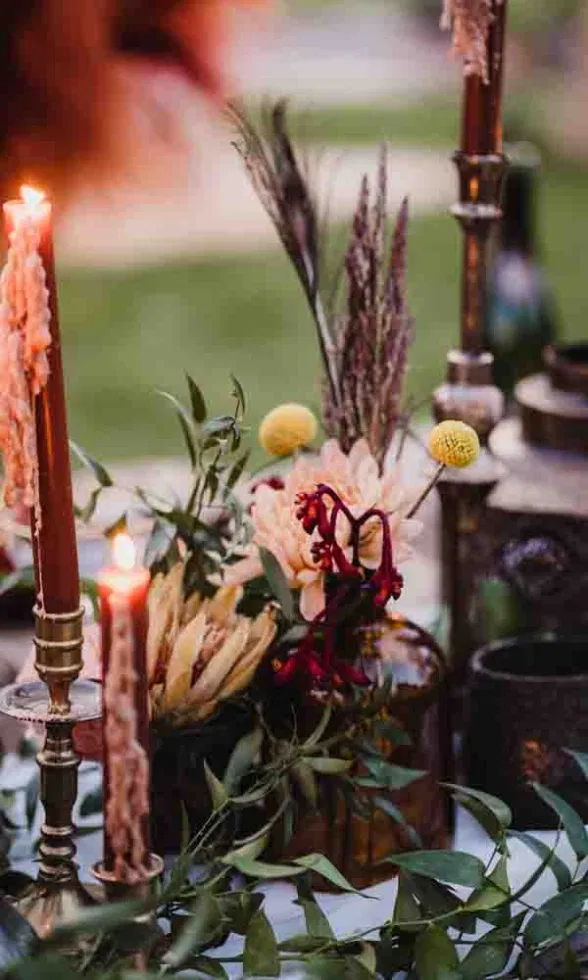 Detailaufnahme der Tischdekoration im Festival-Chic mit Trockenblumen, Kerzen in warmen Farben und natürlichem Greenery.