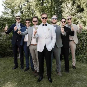 Bräutigam mit seinen Trauzeugen und Freunden im Garten, alle im Anzug und mit Getränken zum Anstoßen.