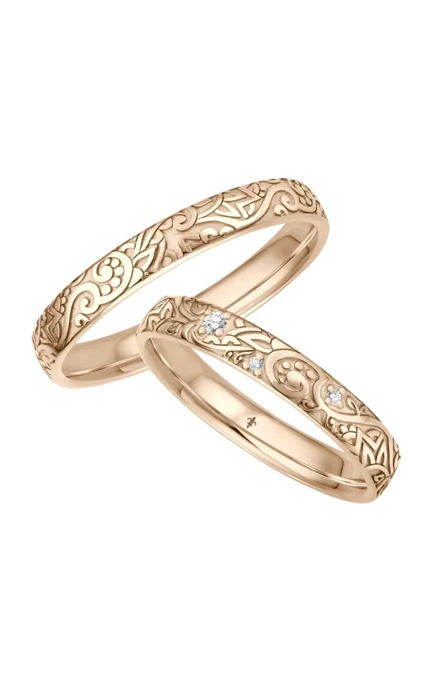 Zwei Eheringe aus Roségold mit kunstvoller Ornamentgravur im Vintage-Stil, einer davon mit mehreren dezent gefassten Diamanten, romantisch und detailreich vor hellem Hintergrund fotografiert.