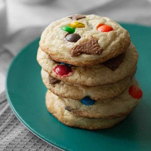 Gestapelte Cookies mit bunten Schokolinsen und Schokoladenstücken auf einem grünen Teller.