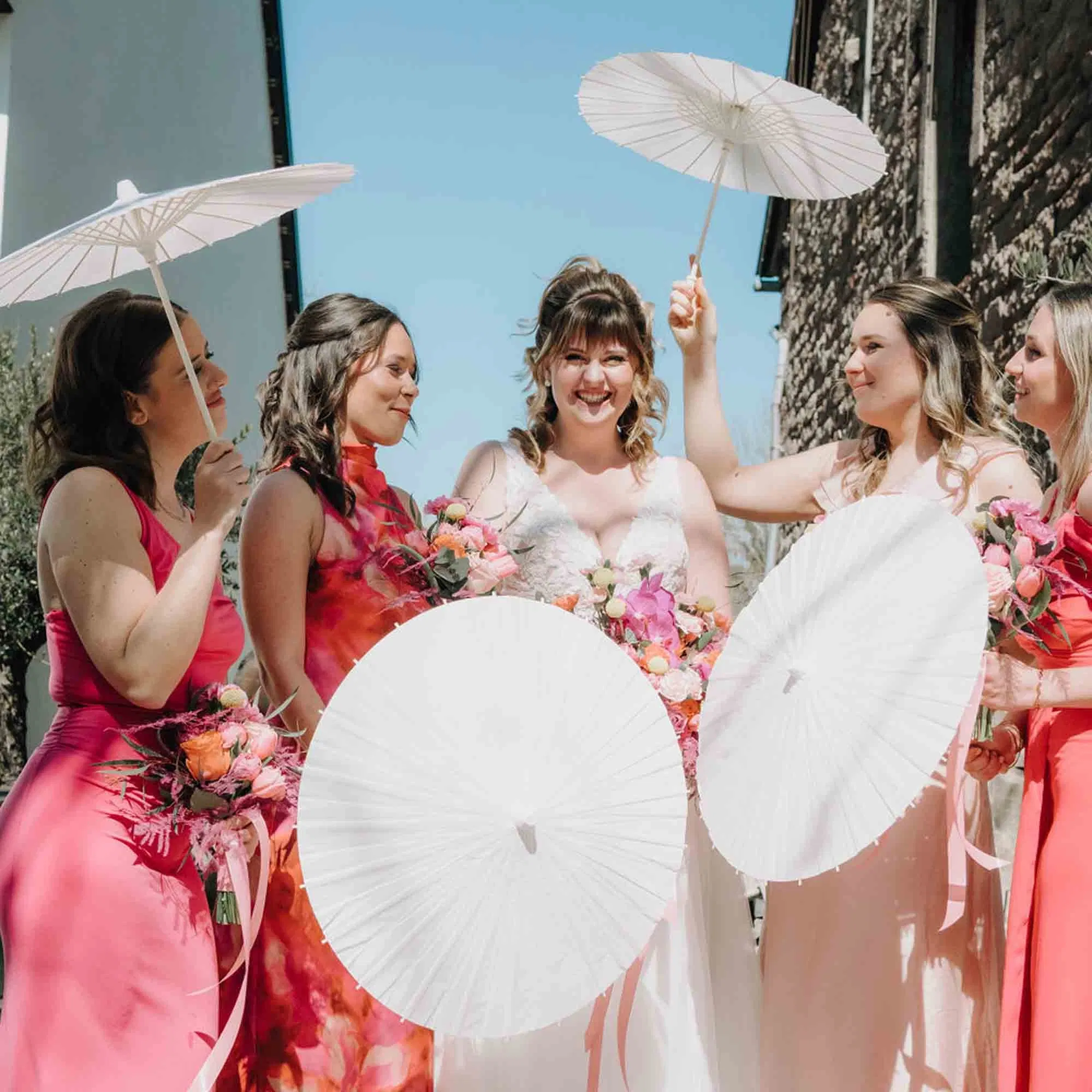 Du: bitte alt text ChatGPT: Ein liebevolles Hochzeits-Porträt eines Brautpaares: Die Braut blickt direkt in die Kamera, trägt ein schlichtes weißes Brautkleid und einen farbenfrohen Blumenanstecker, während sich der Bräutigam nah an sie lehnt und zärtlich seinen Kopf an ihren anlegt. Du: ChatGPT: Gestapelte Coupette-Gläser mit leuchtend orangefarbenem Aperitif und frischen Orangenscheiben als Garnitur, arrangiert als stilvoller Drink-Tower vor grünem, sommerlichem Hintergrund. Du: ChatGPT: Ein fröhliches Brautpaar schenkt gemeinsam Sekt in einen pyramidenförmig aufgebauten Aperitif-Tower mit orangefarbenen Drinks und frischen Zitrusscheiben, vor einer sonnigen Outdoor-Hochzeitskulisse. Du: ChatGPT: Detailaufnahme eines farbenfrohen Brautstraußes in Orange-, Korall- und Rosétönen, arrangiert neben handgerissenen Menükarten mit goldgelbem Rand und eleganter Typografie auf hellem Untergrund. Du: ChatGPT: Detailaufnahme einer sommerlich gedeckten Hochzeitstafel mit Coupette-Glas, Kristallbecher, goldfarbenem Besteck und handgerissener Menükarte auf dem Teller, ergänzt durch Orangen, florale Akzente und warmes Sonnenlicht. Du: ChatGPT: Nahaufnahme eines farbenfrohen Brautstraußes in Pink-, Korall- und Orangetönen, gehalten von der Braut, mit sichtbarem Trauring und zarten Blumenstrukturen vor hellem Hintergrund. Du: ChatGPT: Lange, festlich gedeckte Hochzeitstafel mit orangefarbenen Kerzen, leuchtenden Sommerblumen, frischen Zitrusfrüchten und elegantem Glas- sowie Goldbesteck in sonniger Outdoor-Atmosphäre. Du: ChatGPT: Fröhliche Braut mit ihren Brautjungfern in korall- und rosafarbenen Kleidern, die lachend um sie stehen und weiße Papier-Sonnenschirme halten, vor blauem Himmel und rustikaler Hochzeitskulisse.