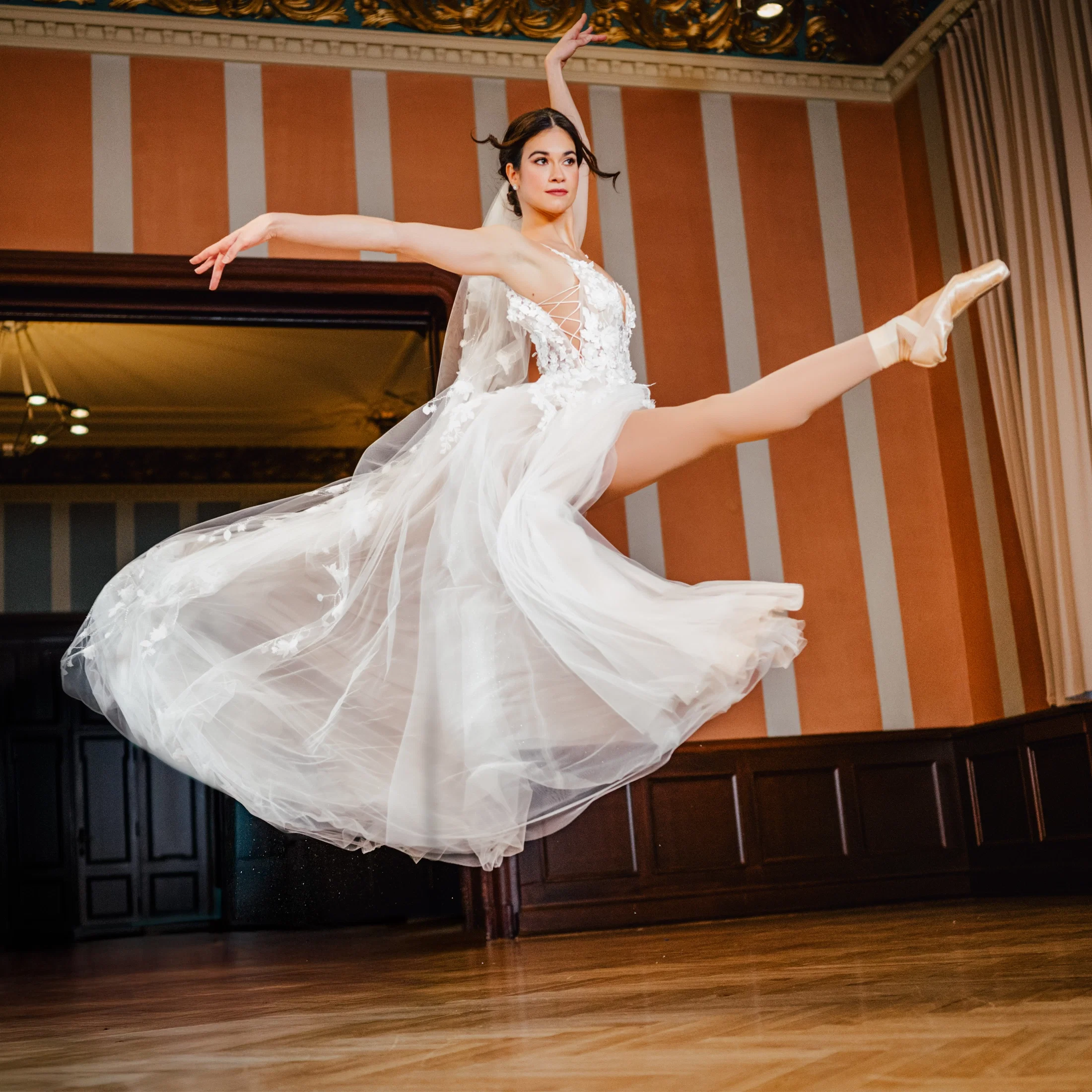 Braut in einem luftigen Tüllkleid springt anmutig durch einen eleganten Saal und erinnert mit ihrer Pose an eine Ballerina.