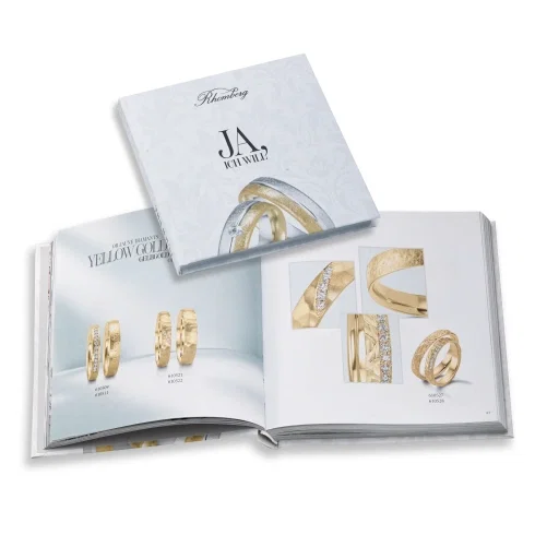 Offenes Schmuck-Katalogbuch mit verschiedenen Eheringen aus Gelbgold sowie geschlossenem Titel „Ja, ich will“.