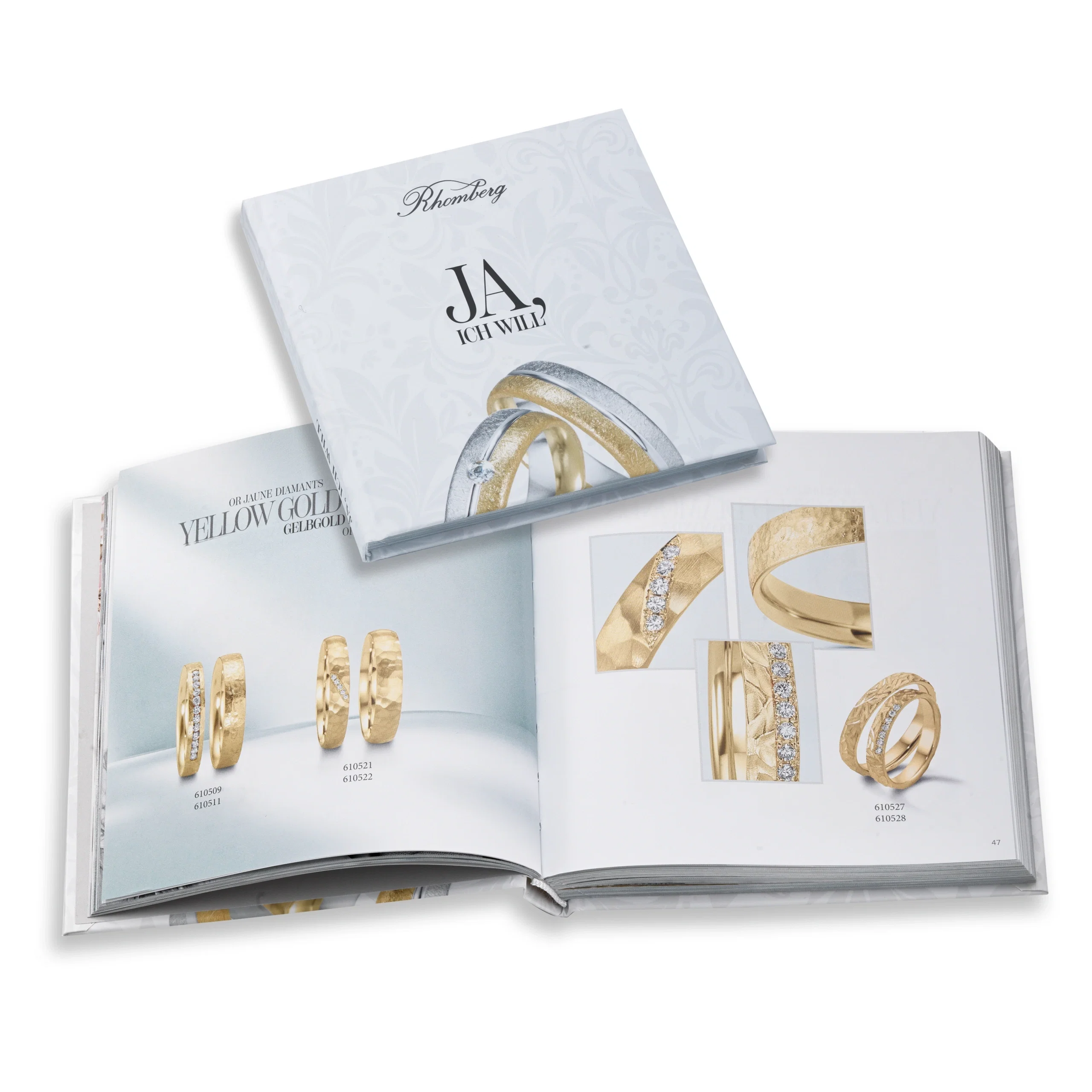 Offenes Schmuck-Katalogbuch mit verschiedenen Eheringen aus Gelbgold sowie geschlossenem Titel „Ja, ich will“.