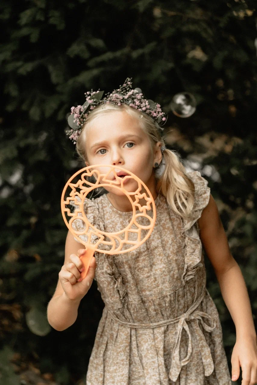 Mädchen mit Blumenkranz pustet konzentriert Seifenblasen und sorgt für verspielte Momente bei der Hochzeit.