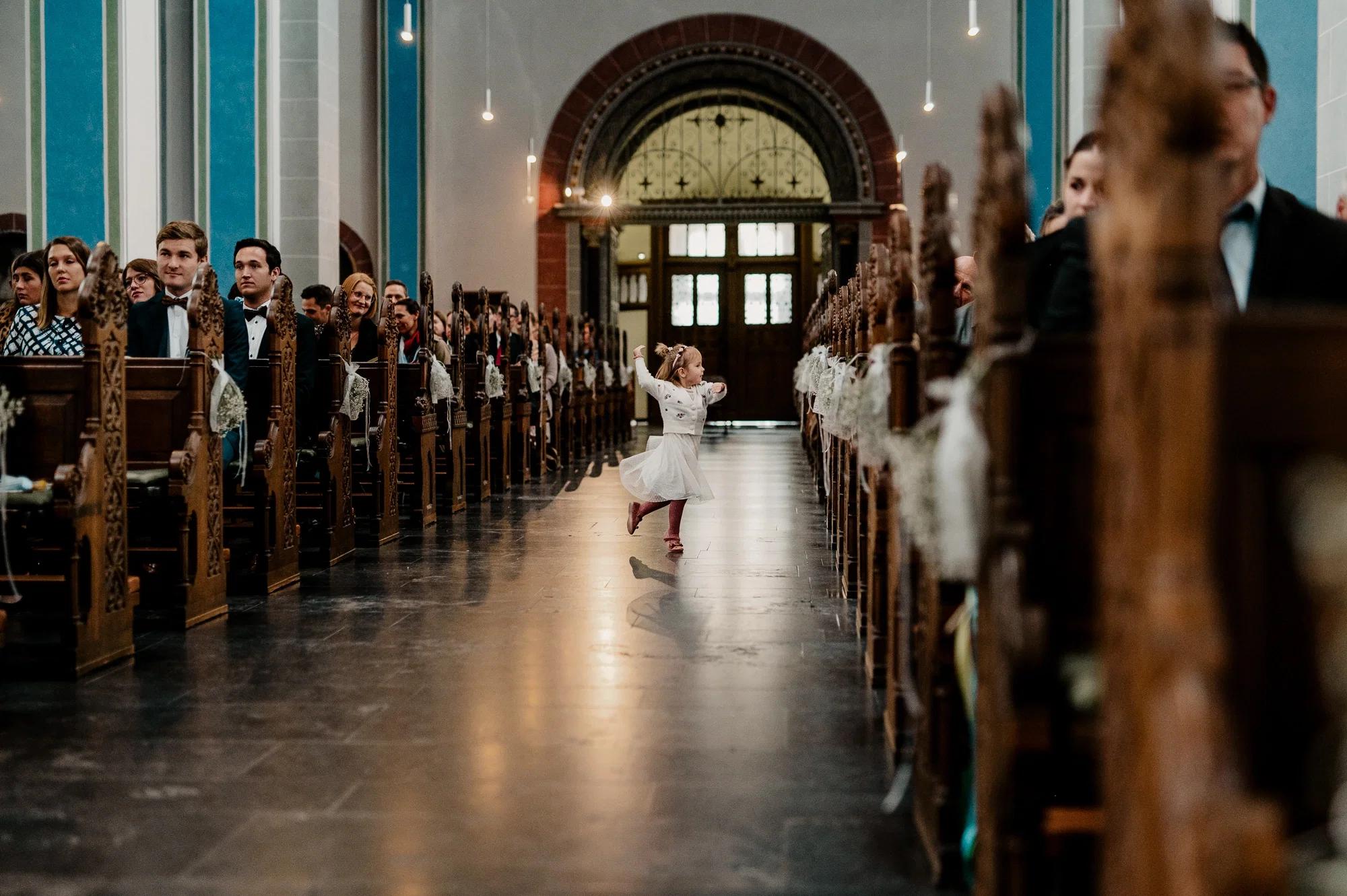 Kleines Mädchen tanzt ausgelassen allein durch den Mittelgang der Kirche und begeistert die Hochzeitsgäste.