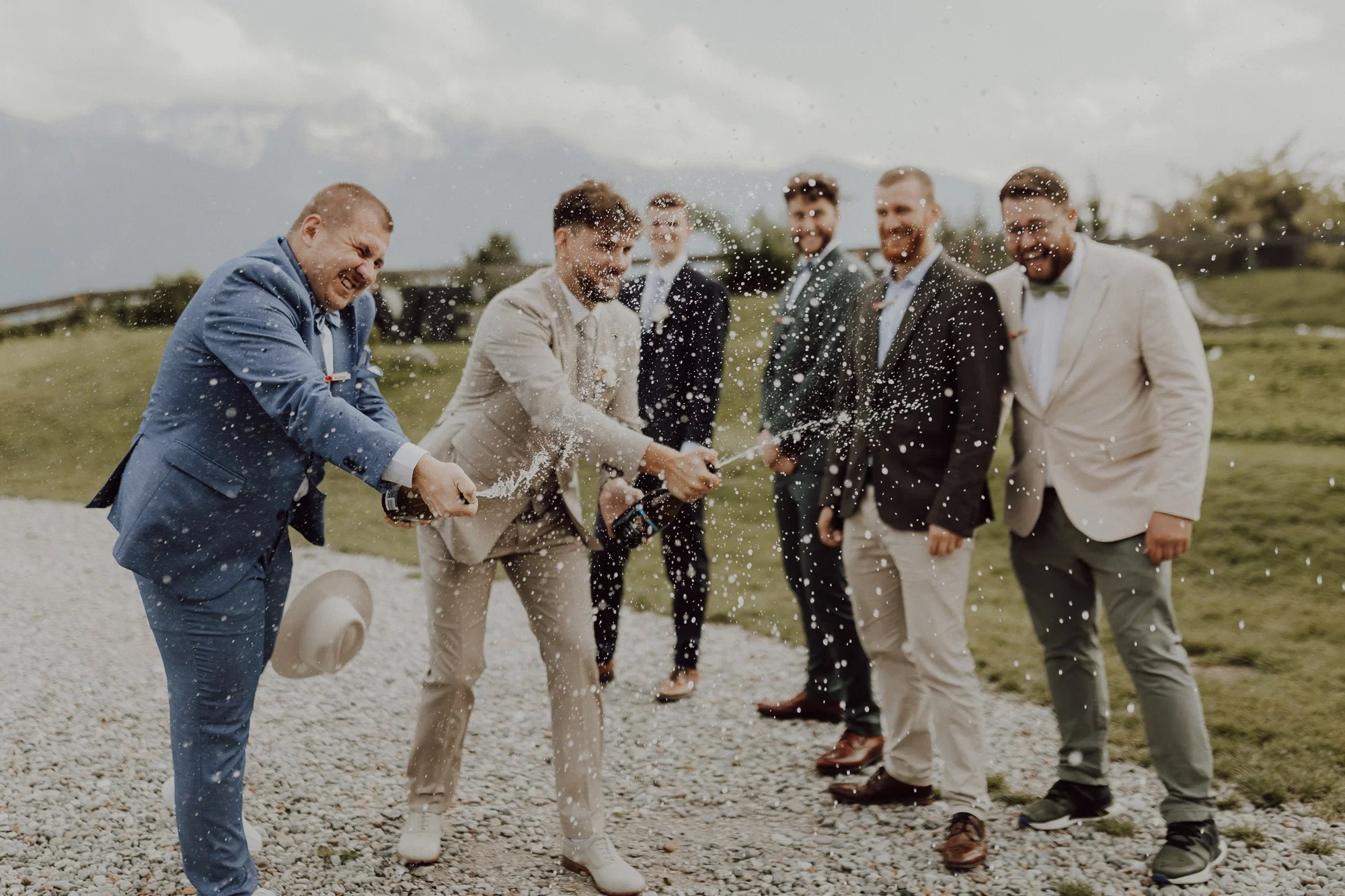 Männergruppe öffnet lachend Champagnerflaschen im Freien, während der Schaum durch die Luft spritzt.