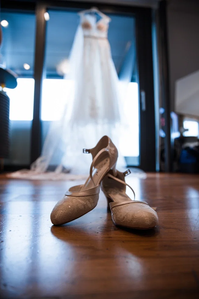 Detailaufnahme von eleganten Brautschuhen vor einem hängenden Brautkleid während des Getting Ready.