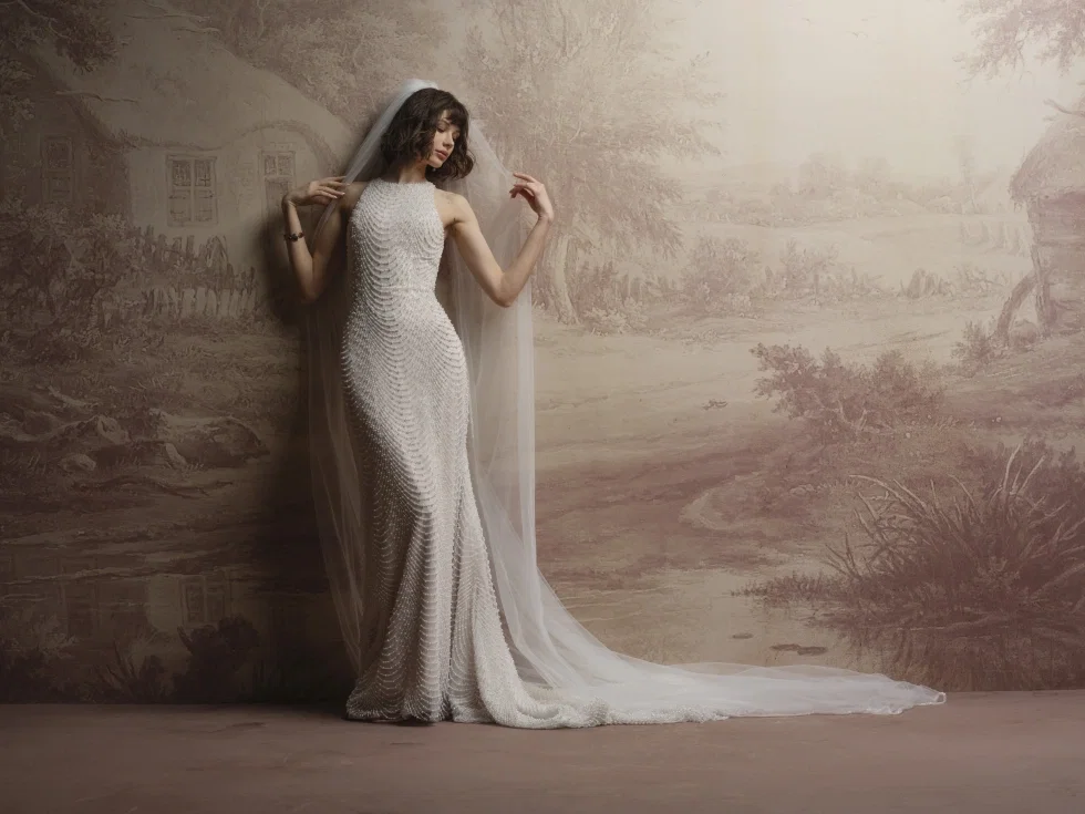 Dieses Kleid von Sottero & Midgley strahlt den Glamour des Old Hollywood aus. Der hohe Ausschnitt sorgt für eine erhabene Ausstrahlung, während die herabhängenden Perlendetails für zusätzliches Licht, Bewegung und Tiefe sorgen.